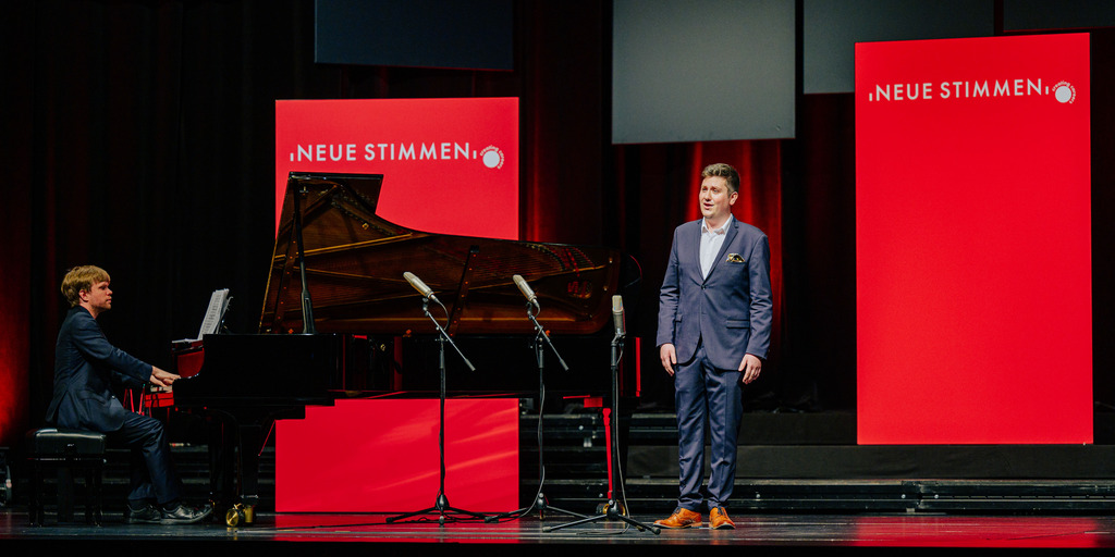 Kieran Carrel, participant of the NEUE STIMMEN 2022 competition, sings on stage during auditions at the final round in Gütersloh. Next to him, a pianist playing the piano can be seen.